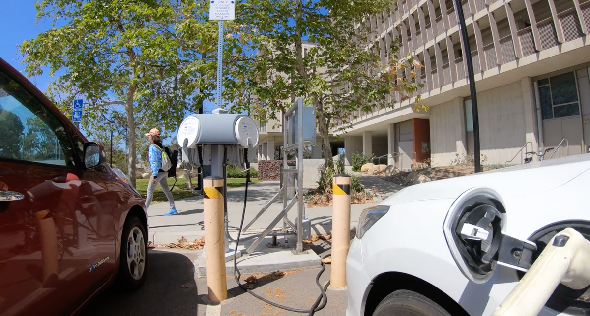 Electric vehicles plugged in to charging stations at UC San Diego's campus with a student walking in the background